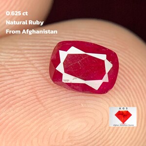 Op de afbeelding: Een kussenvormige natuurlijke robijn uit Afghanistan, met een gewicht van 0,625 ct. De edelsteen heeft een dieprode kleur met een wit geometrisch ontwerp. De tekst "Natural Ruby From Afghanistan" is inbegrepen.