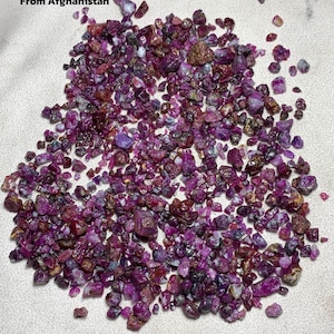 May include: A collection of rough rubies in various shades of red and purple. The image includes text that reads "1348 ct Ruby Rough Lot From Afghanistan."
