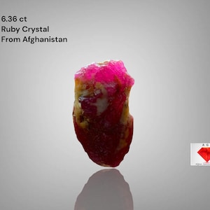 Puede incluir: Cristal de rubí de 6,36 ct de Afganistán. La gema presenta un color rojo intenso con zonas más claras y translúcidas. Incluye el texto "Ruby Crystal From Afghanistan".
