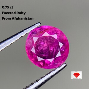 May include: A faceted ruby gemstone, held by tweezers, with the text "0.75 ct Faceted Ruby From Afghanistan." The gem is a vibrant pink color with a starburst pattern of facets. The image also includes a logo for "Afghan Gemstone Source."