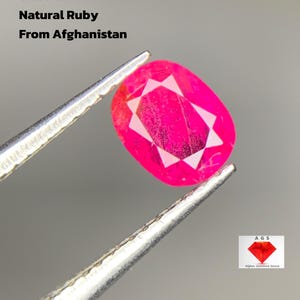 Puede incluir: Un rubí natural de color rosa-rojo brillante, de 0,695 ct, de Afganistán, sujeto con pinzas. La piedra de talla ovalada tiene un llamativo patrón interno. El texto de la imagen dice "Natural Ruby From Afghanistan".
