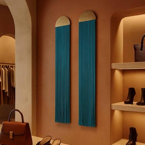 May include: A retail display featuring a brown leather handbag with a gold clasp, black heeled mules, and leather belts. Teal wall hangings with gold accents and shelves with shoes are visible. The store has a neutral color palette.