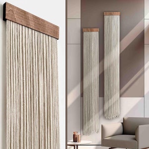 Può includere: Due arazzi in macramé beige con listelli in legno, appesi a una parete marrone chiaro in un soggiorno moderno con una poltrona beige e un tavolino.