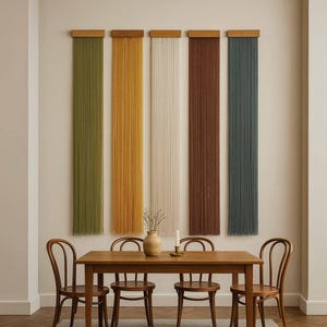 May include: A dining room scene featuring a wooden table and four chairs. Above the table, five vertical wall hangings in olive green, yellow, cream, brown, and teal are displayed. A vase and candle sit on the table.