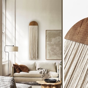 May include: A white sofa with brown throw pillows in a living room with a wooden coffee table and a macrame wall hanging with a wooden top.
