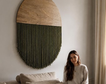 May include: A wall-mounted decorative piece featuring a semi-circular light wood top panel with a natural grain, paired with a long, dense fringe of dark olive green yarn hanging vertically to form a rounded shape against the wall.