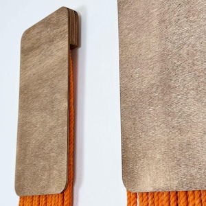 May include: Two wooden wall hangings with orange rope fringe. The wood is a light brown colour and has a wood grain texture.