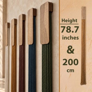 Pode incluir: Uma série de cinco suportes de madeira montados na parede, cada um com uma longa franja vertical de cordões pendentes em branco, mostarda, bordô, azul-marinho e verde-oliva. O texto indica uma altura de 78,7 polegadas e 200 cm.