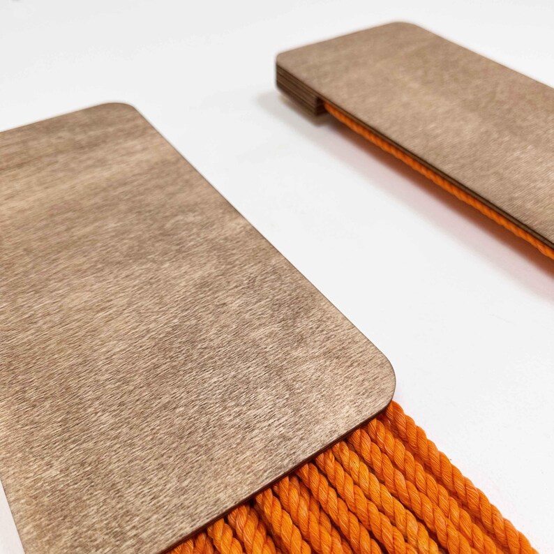 May include: Two wooden wall hangings with orange rope fringe. The wood is a light brown colour and the rope is a bright orange.