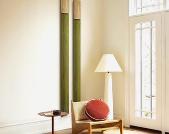 May include: Two green wall hangings with wooden frames hang on a white wall. A wooden chair with a red cushion sits in front of the wall hangings. A lamp with a white shade stands next to the chair. A small round table with a black tray sits in front of the chair.