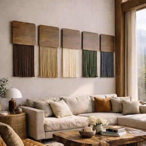Könnte beinhalten: Fünf quadratische Wandbehänge aus Holz mit Fransen in Braun, Beige, Creme, Grün und Grau. Die Wandbehänge sind über einem beigefarbenen Ecksofa mit dekorativen Kissen angebracht. Ein Couchtisch aus Holz und eine Lampe befinden sich im Vordergrund.