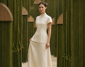 May include: A cream-coloured two-piece ensemble consisting of a short-sleeved top with a high mock neck and a matching floor-length skirt. The top features a fitted bodice that extends slightly over the waistline of the long, flowing skirt.