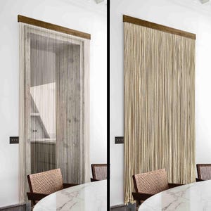 May include: A doorway curtain composed of vertical beige strands, attached to a dark brown wooden header. The curtain obscures a doorway, revealing a glimpse of the room behind. The room includes a marble table and woven chairs.