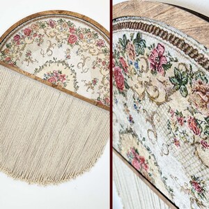 May include: A half-circle wall hanging with a floral patterned fabric framed in wood and a long fringe of white yarn.
