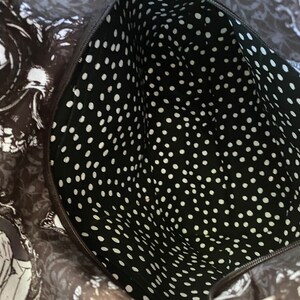 May include: Black and white polka dot fabric lining the inside of a bag. The fabric is smooth and has a subtle sheen.