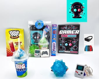 May include: A gamer themed gift box with a blue and green slushie cup, a blue and green stress ball, a black and white gamer fun book, a black and blue VR headset, a black and red video game controller, a green and black handheld video game, a blue and green push pop, and a blue and green candy stick.