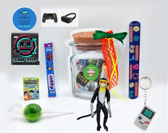 May include: A glass jar filled with small toys and stickers, including a monkey figurine, a green lollipop, a pack of trading cards, a candy bar, a keychain with a video game console, a sticker with the text "Game Over", and a sticker with the text "Love Gaming".