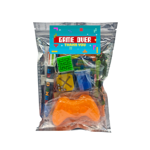 May include: A clear plastic bag filled with party favours for a video game themed party. The bag includes a small orange plastic video game controller, a blue slime container, a green and yellow maze toy, a small plastic container of silver balls, a red and yellow plastic X toy, a green and yellow plastic ninja turtle toy, and a blue and yellow plastic pencil. The bag has a blue and yellow label that says "Game Over Thank You".