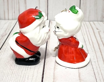 Könnte beinhalten: Zwei Weihnachtsornamente aus Keramik. Einer ist der Weihnachtsmann mit rotem Hut und Anzug, weißem Bart und schwarzen Stiefeln. Der andere ist Frau Claus, in einem roten Kleid und weißen Haaren. Beide haben grüne Stechpalmenakzente.