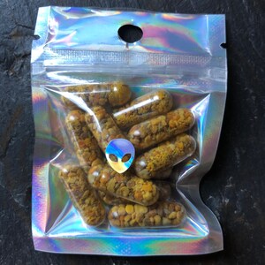 May include: A clear plastic bag with a silver iridescent finish contains a large quantity of yellow and brown capsules. The bag has a hole at the top and a silver alien sticker.