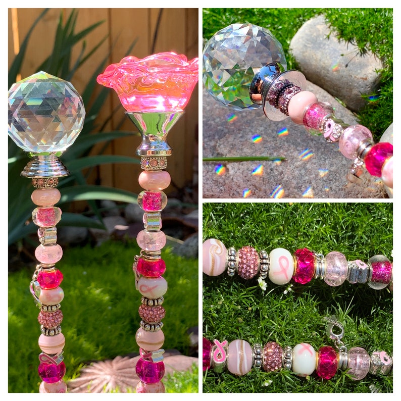 May include: Two pink and silver garden stakes with crystal tops and pink beads. The stakes are decorated with pink ribbon charms and pink and silver beads. The stakes are on a green grass background.