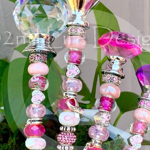 May include: Four pink and silver beaded charm bracelets with different crystal tops. The charms include pink ribbons, hearts, and beads. One charm says "HOPE".