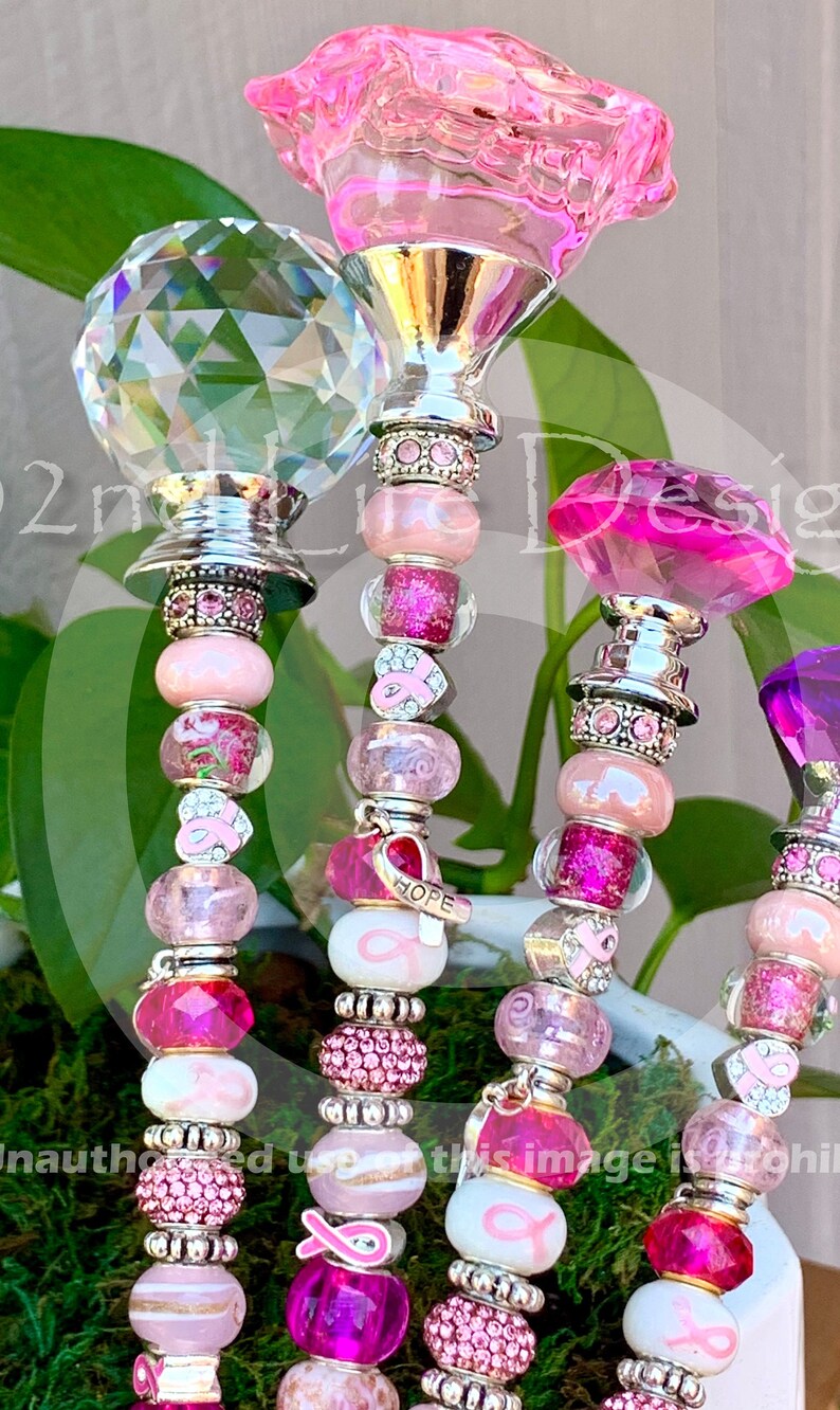 May include: Four pink and silver beaded charm bracelets with different crystal tops. The charms include pink ribbons, hearts, and beads. One charm says "HOPE".