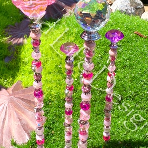 May include: Four decorative garden stakes with pink, white, and clear beads. The top of each stake features a different topper: a pink flower, a clear crystal ball, a pink crystal, and a purple crystal.