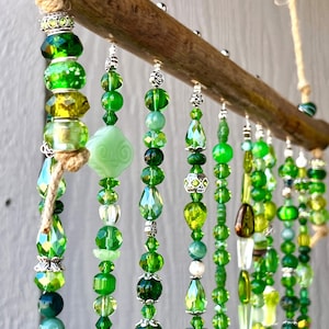 May include: A green beaded wind chime with a wooden top and silver beads. The wind chime has multiple strands of beads in various shades of green.
