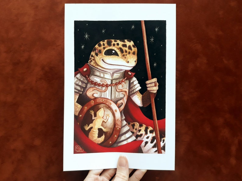 May include: A watercolor painting of a gecko wearing armor and holding a spear. The gecko is wearing a red cape and has a shield with a smaller gecko on it. The background is a dark blue with stars.