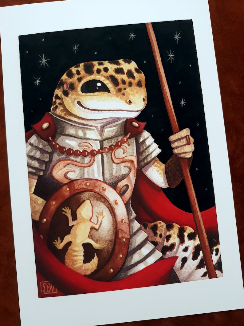 May include: A watercolor painting of a gecko wearing armor and holding a spear. The gecko is standing in front of a dark blue background with white stars. The gecko is wearing a red cape and a shield with a smaller gecko on it.