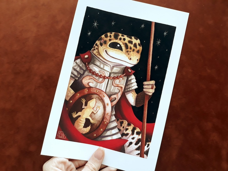 May include: A cartoon illustration of a gecko wearing armor and a red cape, holding a spear and a shield with a smaller gecko on it. The background is a dark blue with white stars.