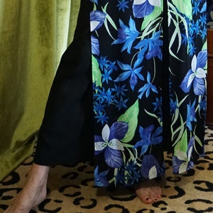 May include: Black palazzo pants with a floral print featuring blue and white flowers and green leaves. The pants have a wide leg design and a high waist. The floral pattern is set against a black background.