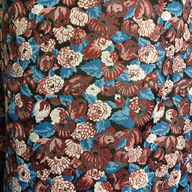 Puede incluir: Primer plano de una tela con un estampado floral. El dise&ntilde;o presenta una mezcla de flores rojas, blancas y rosas, sobre un fondo azul y negro. La tela tiene una impresi&oacute;n densa y completa, creando una apariencia texturizada.