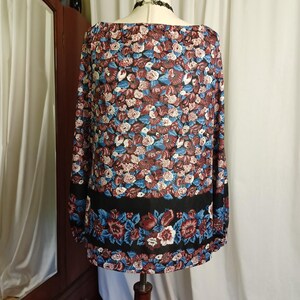 Puede incluir: Una blusa de manga larga con un estampado floral en burdeos, azul y blanco. La blusa tiene una banda negra en la parte inferior con un dise&ntilde;o floral. El escote es ancho y la tela parece ligera.