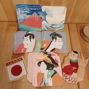 May include: A collection of Japanese-themed coasters and a patch. The coasters feature iconic Japanese art, including Mount Fuji, a wave, and portraits. The patch displays the Japanese flag with the word "JAPAN".