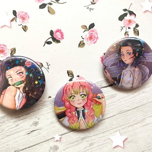 Può includere: Tre spille rotonde con personaggi anime. La prima spilla presenta una ragazza con i capelli rosa e gli occhi verdi, la seconda spilla presenta una ragazza con i capelli neri e gli occhi blu, e la terza spilla presenta una ragazza con i capelli neri e gli occhi rosa.