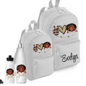 May include: White backpacks and water bottles with a black graphic of a woman with a crown of hair, a peace sign, and a gold heart. The backpack has the name "Evelyn" in cursive. The water bottles have the name "Jailah".