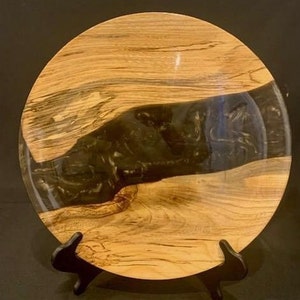 May include: A round wooden platter with a black resin inlay. The wood has a natural grain pattern and the resin is smooth and glossy.