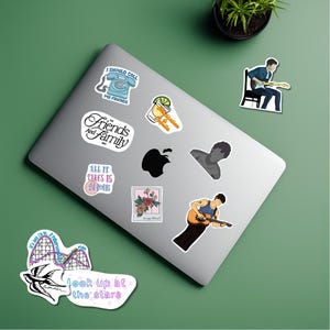 Könnte beinhalten: Ein Laptop mit verschiedenen Aufklebern. Aufkleber zeigen ein Telefon, einen Cocktail, eine Achterbahn, ein Blumendesign und Text mit der Aufschrift "Friends and Family" und "Look up at the stars".