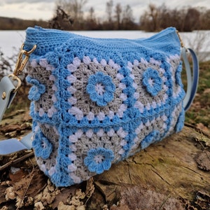 May include: A blue and gray crocheted bag with a flower design. The bag has a zipper closure and a long strap.