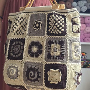 Könnte beinhalten: Handgefertigte Häkeltasche mit Patchwork-Design. Die Tasche hat verschiedene quadratische Muster in Beige-, Grau- und Brauntönen. Sie hat Bambusgriffe und einen cremefarbenen Rand. Ein stilvolles und praktisches Accessoire.