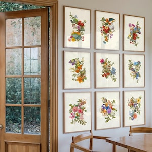 Op de afbeelding: Een galerijwand met negen ingelijste prints met botanische illustraties van kleurrijke bloemenboeketten. Elke rechthoekige lijst bevat een uniek arrangement van rode, gele, blauwe, roze en oranje bloesems op een crèmekleurige achtergrond.