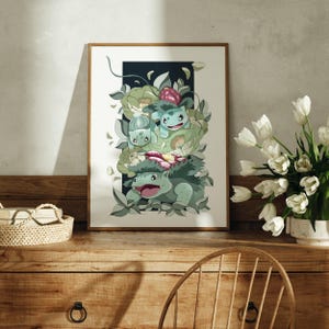 May include: A framed art print featuring a vertical illustration of three green creatures in various stages of evolution, surrounded by stylized light green leaves and pink flowers against a dark rectangular background with white borders.