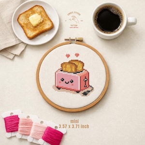 Op de afbeelding: Een kruissteekborduurring met een roze broodroosterontwerp, 9,07 x 9,42 cm, met een lachend gezicht en twee sneetjes toast. De afbeelding toont ook een bord toast met boter, een kopje koffie en spoelen roze garen. De tekst luidt "CROSS STITCH PATTERN made with love".