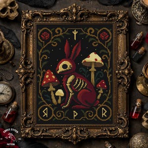 May include: Cross-stitch pattern of a red rabbit skeleton with mushrooms, framed in an ornate gold frame. The design includes a black background with a gothic aesthetic, featuring the text "Cross Stitch Pattern".