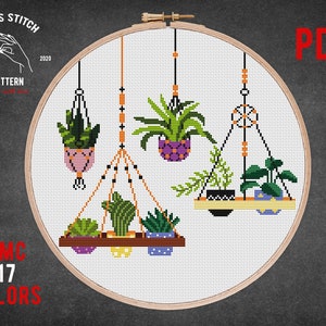 May include: Cross stitch pattern featuring a set of hanging plants in macrame planters. The pattern includes 17 colors and is available as a PDF download.  The pattern is displayed in a wooden embroidery hoop.