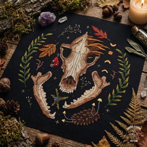 May include: A black cross-stitch design depicting an animal skull encircled by autumnal leaves, sprigs, and mushrooms. The pattern includes a small red butterfly. The words "Cross Stitch Pattern" are in the bottom right corner, set against a dark background.