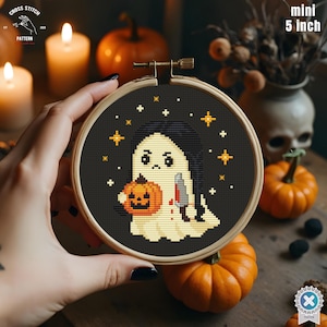 May include: A mini 5-inch cross-stitch embroidery hoop featuring a Halloween ghost design. The ghost holds a pumpkin and a bloody knife, surrounded by stars on a black background. The design is set in a wooden hoop.