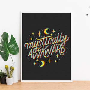 May include: Cross stitch pattern featuring the phrase "mystically awkward" in a retro, pixelated style with a rainbow color scheme. The design is surrounded by stars and crescent moons on a black background.
